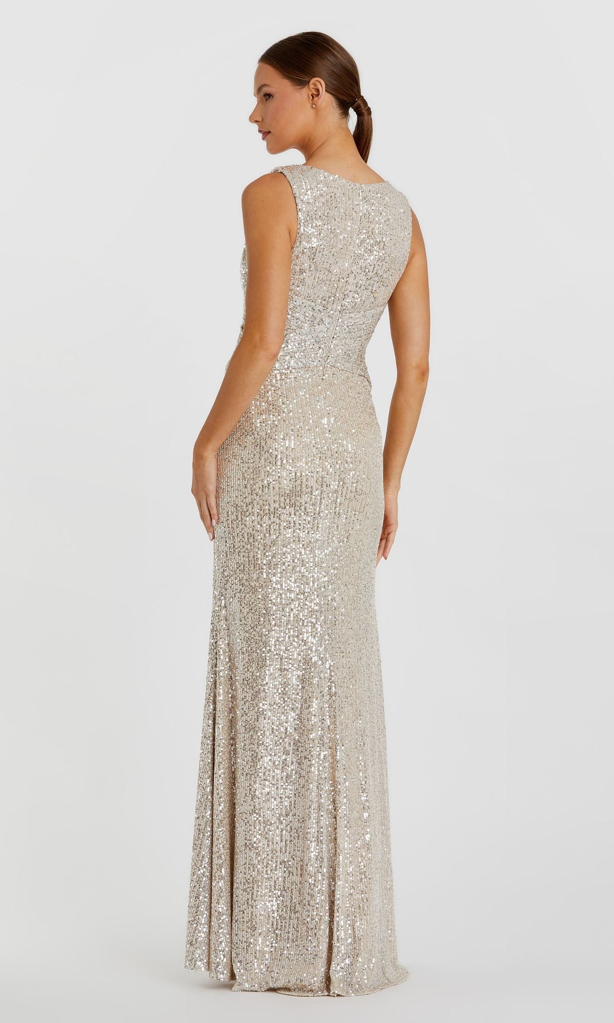 A woman models the Mac Duggal 26598, a sleeveless, floor-length silver sequin formal dress, standing with her back and side to the camera against a plain white background.